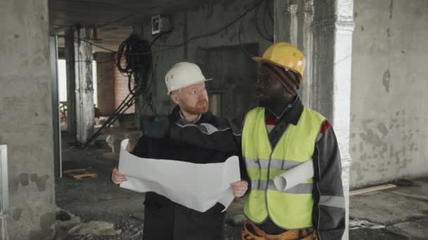 Kaukasisk Ingenjör Och Afroamerikansk Förman Håller Ritning Diskuterar Arbetsplan Byggarbetsplatsen — Stockvideo
