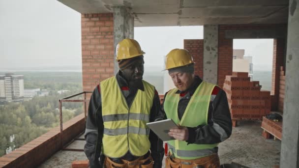 Etnisk Mangfoldige Bygningsarbeidere Som Ser Blåkopier Digital Nettbrett Diskuterer Plan – stockvideo