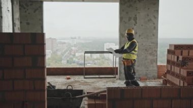 İnşaat alanı boyunca yürüyen ve çalışma planını tartışan iki farklı etnik kökenli inşaat işçisinin uzun bir görüntüsü.