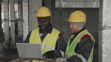 İnşaat alanında çalışan Afro-Amerikan mühendis ve Kafkasyalı ustabaşı laptoptaki verileri kontrol ediyor ve sorunları tartışıyorlar.