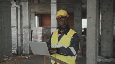 Genç, Afro-Amerikan inşaat işçisi üniformalı, şapkalı, laptoptan mesaj atan.
