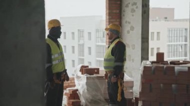 Foreman yeni işçiyle tokalaşıyor. Sonra ona inşaat alanını gösterecek.