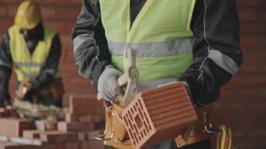 Seçici odak noktası, tanınmayan inşaat işçisinin ekstra tuğla uzunluğunu kırmak için çekiç kullanması.