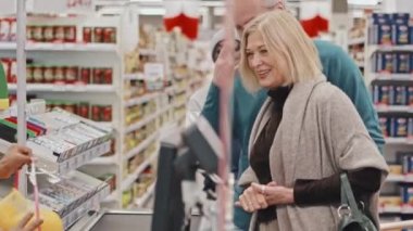 Afro-Amerikalı kadın kasiyer markette kuyrukta bekleyen müşterilere servis yaparken meyve ve sebze tartıyor.
