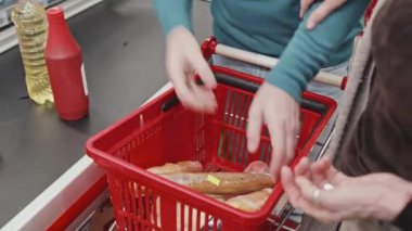 Müşteriler alışveriş sepetindeki gıda ürünlerini süpermarkette kontrol ederken taşıma bandına yerleştiriyorlar.