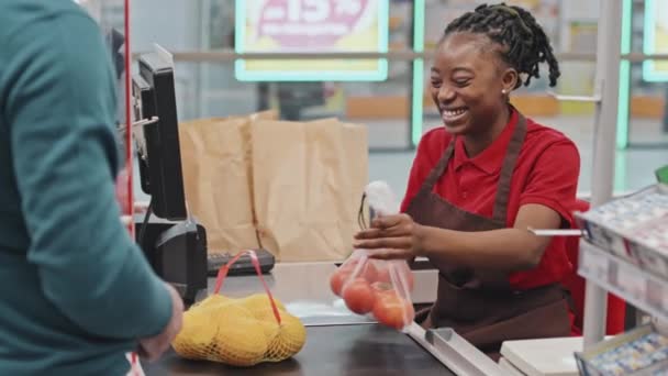 アフリカ系アメリカ人女性のレジ係が現金カウンターに座っているスーパーでのチェックアウト時にクレジットカードで支払う顧客 — ストック動画