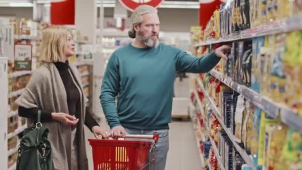 在超级市场选择意大利面的时候 中年白种人夫妇背着购物车 带着食品货架散步 — 图库视频影像