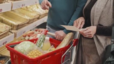 Alışveriş arabalı birkaç müşterinin alışveriş listelerine göre süpermarkette yemek alışverişi yaparken çekilmiş görüntüleri.