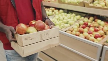 Tanınamayan Afro-Amerikan erkek süpermarket işçisinin taze elmalarla ahşap palet taşıyıp raflarda sergilediği görüntüler.