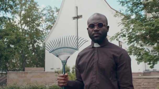Kilisenin Arka Bahçesinde Elinde Tırmıkla Duran Afrika Kökenli Katolik Rahibin — Stok video