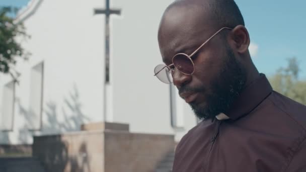 非洲裔美国牧师站在室外阅读圣经或祈祷书的中等特写倾斜 — 图库视频影像