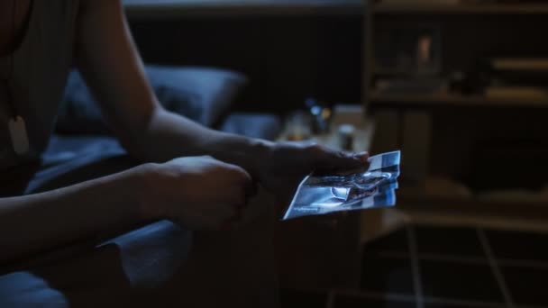 戦争で亡くなった友人の写真を見て夜にベッドの上に座っている若い軍人の中程度のクローズアップ — ストック動画