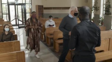 Koruyucu maske takan Afrikalı Amerikalı rahip ziyaretçileri selamlıyor ve Pazar ayinine Katolik kilisesinde başlıyor.
