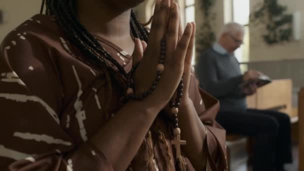 カトリック教会で神へのロザリオの祈りを持っている若いアフリカ系アメリカ人女性のクローズアップを傾ける — ストック動画