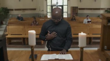 Katolik kilisesinde sunağın önünde durup Tanrı 'ya dua eden Afrikalı genç bir papaz.