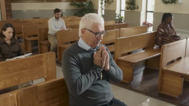 カトリック教会のベンチに座って神に祈るロザリオを保持しているシニア白人男性の中肖像 — ストック動画