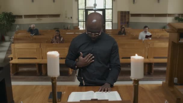 カトリック教会の祭壇の前に立つ若い大人のアフリカ系アメリカ人牧師は神への祈りと言っています — ストック動画