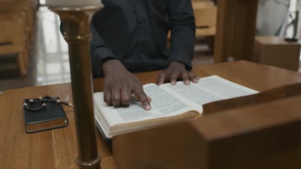 无法辨认的非裔美国天主教牧师站在教堂的祭坛前诵读圣经或祈祷书 — 图库视频影像