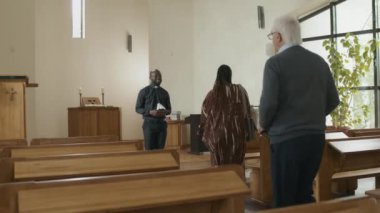 Genç Afrikalı Amerikalı rahip Katolik kilisesinde Pazar ayinine katılanları selamlıyor.