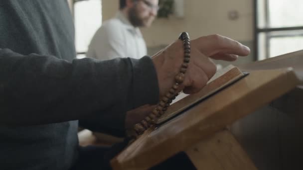 ロザリオの朗読の祈りの本や教会の聖書を保持している認識できない成熟した男性の選択的焦点のクローズアップ — ストック動画