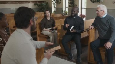 Kilisede bankta oturmuş cemaate İncil hikayesini anlatan genç, yetişkin Afrikalı Amerikalı Katolik papaz.
