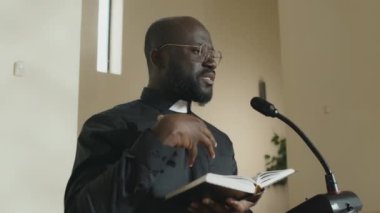 İncil 'i elinde tutan modern, genç Afrikalı Amerikalı rahip mikrofonla kürsüde vaaz veriyor.