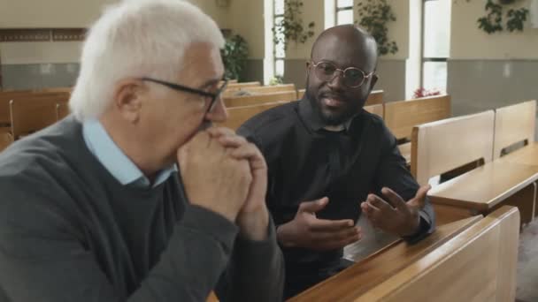 아프리카 미국인 가톨릭 사제는 교회에서 의자에 앉아서 원로에게 무엇인가를 설명하거나 — 비디오