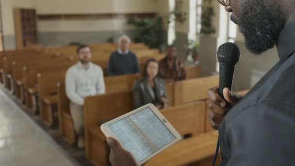 現代カトリック教会の牧師がデジタルタブレットを持っていて 聖書の本が画面上で説教されている様子を撮影したものです — ストック動画
