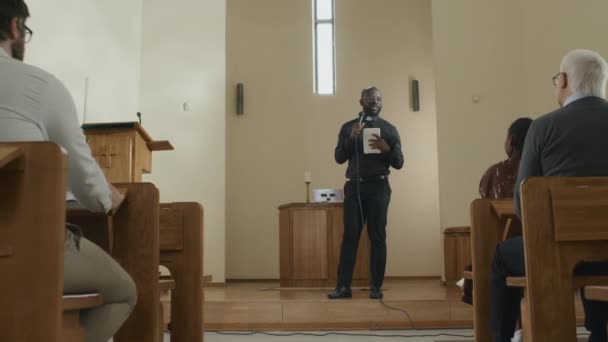 年轻的非洲裔美国牧师拿着数字平板电脑和话筒在教堂里向一群教区居民说教时拍了很长时间的多莉 — 图库视频影像