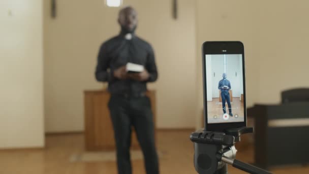 現代アフリカ系アメリカ人カトリック聖職者の選択的焦点スマートフォンを使用して説教のビデオを記録する — ストック動画