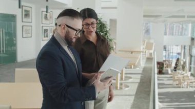 İş çifti iş yerinde dijital tablet kullanıyor ve modern ofiste dururken online sunumu tartışıyor