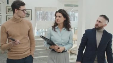 Bir grup genç iş arkadaşının ofis koridorunda yürürken sohbet ederken çekilmiş görüntüleri.