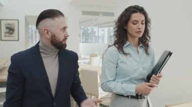 Genç kendine güvenen işadamının modern ofis koridorunda yürürken asistanına talimat verirken görüntüsü.