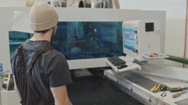 Mobilya fabrikasında modern ekipmanlarla çalışırken ahşap bitirme makinesinden tahta alan adam.