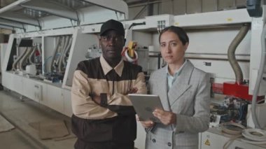 Beyaz kadın müdürün tabletli ve Afro-Amerikan işçiyle birlikte mobilya fabrikasında fotoğraf çektirirken belini kaldır.