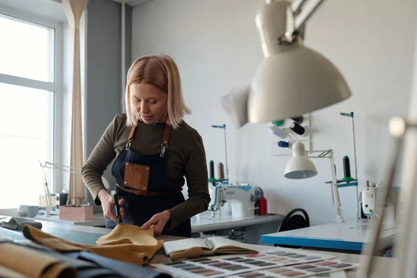 生地サンプルやその他の消耗品と開いてノートブックで革のテーブルを切断服のプロの女性デザイナー — ストック写真