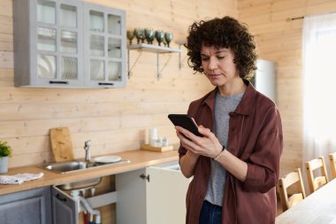 Genç sorunlu ev hanımı, tamir servisini ararken mutfak tezgahına kırık muslukla akıllı telefondan kontak yapıyor.