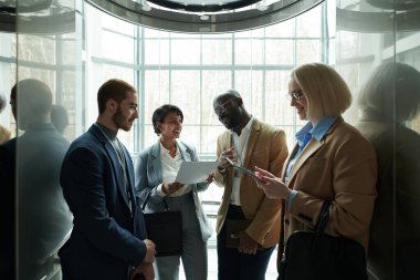 Bir grup başarılı kültürler arası resmi kıyafet delegesi asansörde dikilip yukarı çıkarken konferansa hazırlanıyorlar.