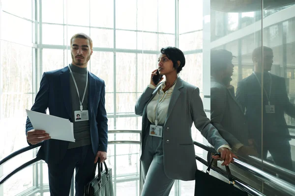 在电梯里 年轻的男性代表站在女同事旁边 穿着便服在智能手机上交谈 一边看报告要点 — 图库照片
