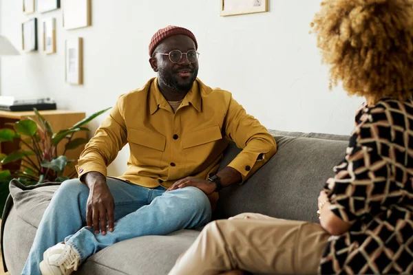 年轻自信的非洲裔美国男性经理在谈话时坐在沙发上看着女同事 — 图库照片