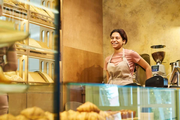 パン屋のカウンターデスクで制服姿の若い陽気な女性と同僚やパン屋を見て新鮮なパンを展示 — ストック写真