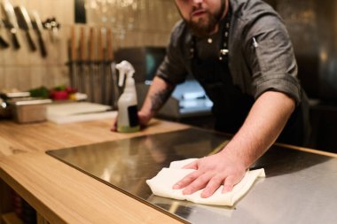 İş yerinde eğilmeden önce elektrikli ocağı sterilize eden ve temizleyen genç profesyonel şefe yakın plan.