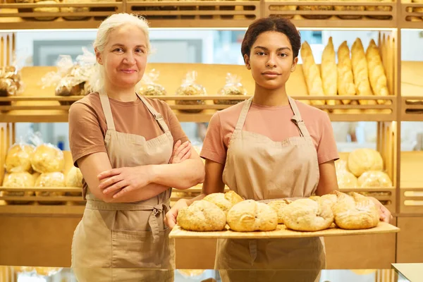 Две Межкультурные Пекари Продавщицы Булочной Униформе Глядя Камеру Стоят Витрины — стоковое фото