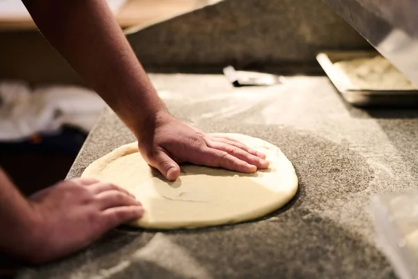 年轻厨师的手在桌上用新鲜面团做扁平面包 同时站在厨房的工作场所 为客人做披萨 — 图库照片