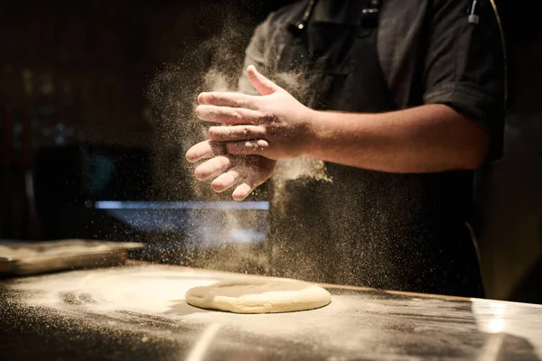 厨师们的特写镜头 一边站在餐桌旁 一边在面团上洒上新鲜面粉 一边为自己餐厅的客人们准备意大利披萨 — 图库照片