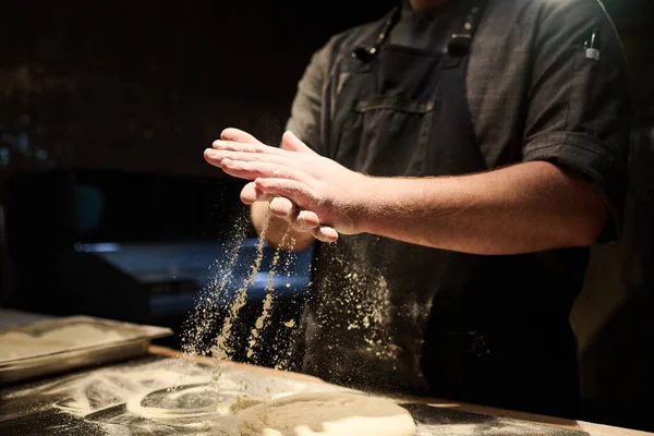 年轻厨师的手在手掌间揉搓面粉 用新鲜面团撒在桌子上 然后揉碎 做披萨 — 图库照片