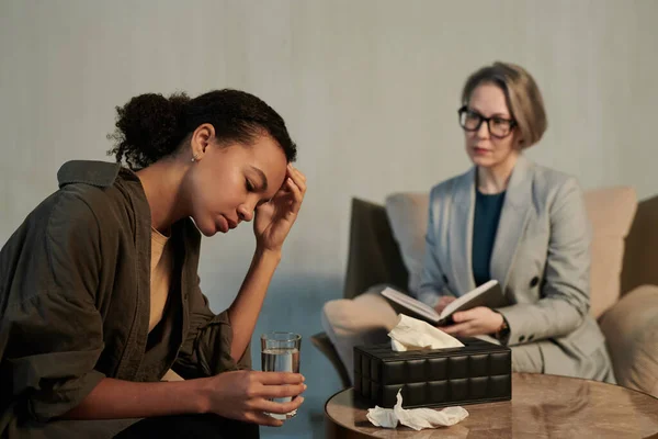 一位年轻的非洲裔美国女性咨询师 手里拿着一杯水 在办公室里向心理治疗师描述她的问题 — 图库照片