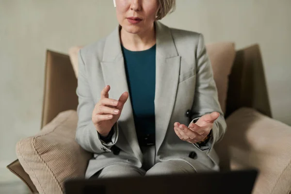 网上聊天期间 穿着灰色西装坐在笔记本电脑前扶手椅上的自信心理学家的特写 并为病人提供建议 — 图库照片