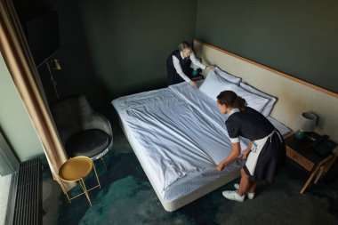 Genç oda hizmetçisi ve yönetici açısının üstünde misafirler için çift kişilik yatak hazırlarken gezginler gelmeden önce yatak örtülerini değiştiriyorlar.