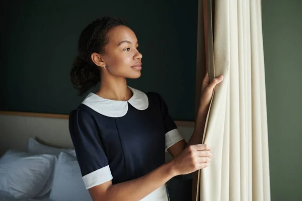 Junges Hübsches Hausmädchen Dunkelblauem Kleid Öffnet Morgens Vorhänge Hotelzimmer Während — Stockfoto